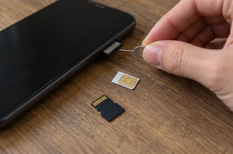 Een simkaartlade wordt met een uitwerppennetje uit een uitgeschakelde smartphone gehaald, met een simkaart en geheugenkaart op tafel