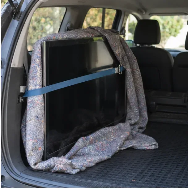 Platte televisie rechtop vastgezet in de laadruimte van een auto met een spanband en zachte deken