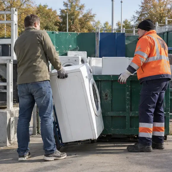 Een bewoner brengt een oude wasmachine met hulp van een medewerker naar een container voor grote apparaten bij een recyclingpunt