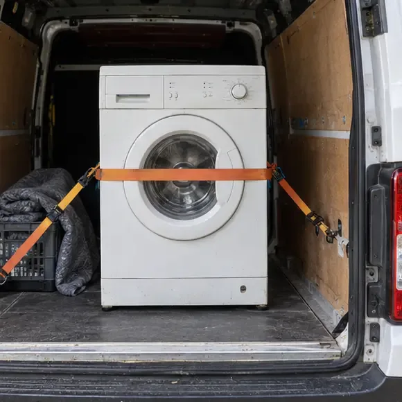 Een oude wasmachine staat rechtop en is met spanbanden vastgezet in de laadruimte van een bestelbus