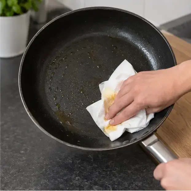 Een hand veegt de laatste vetresten met keukenpapier uit een koekenpan