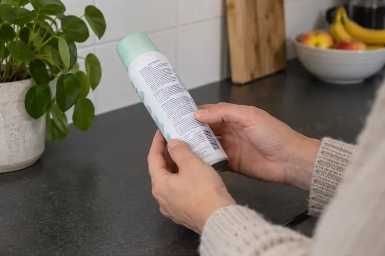Iemand bekijkt het etiket van een spuitbus om het product en de afvalroute te herkennen