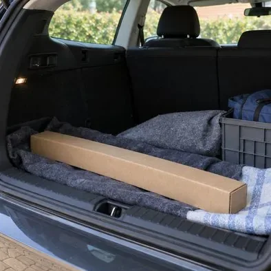 Een lange kartonnen koker met een tl-buis ligt vast en plat in de kofferbak van een auto.