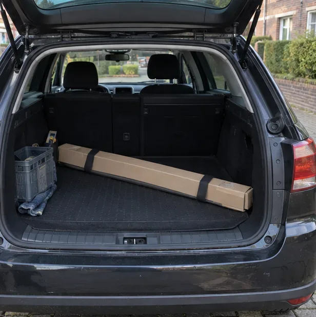 Een lange kartonnen koker met een tl-buis ligt recht in de bagageruimte van een auto.