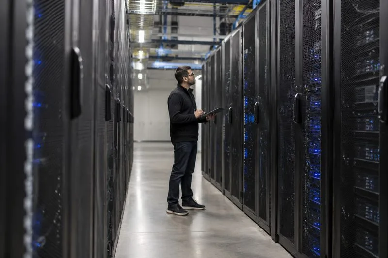 An engineer holding a tablet while inspecting server racks in a data center aisle