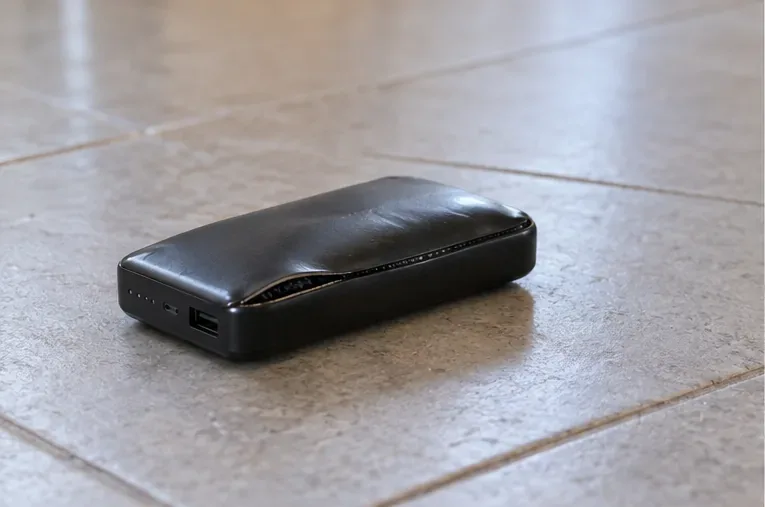 Batería externa visiblemente abombada sobre una baldosa, con el cable desconectado a un lado.