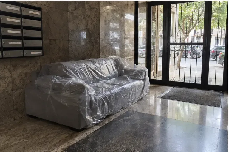 Un sofá protegido espera dentro del portal, junto a la entrada y sin bloquear el paso