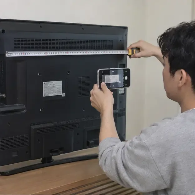 거주자가 TV 뒷면의 정보 라벨을 확인하면서 줄자로 가로 크기를 측정하는 모습