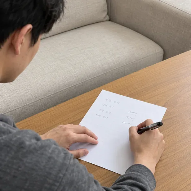 소파 옆에서 종이에 배출 관련 내용을 적는 사람