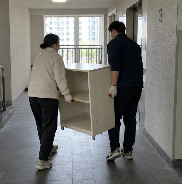 두 사람이 아파트 복도에서 큰 수납장을 안전하게 옮기고 있다