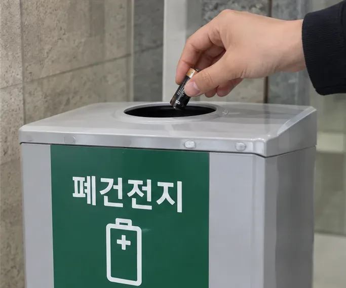 폐건전지라고 표시된 전용 수거함에 사용한 건전지를 넣는 손