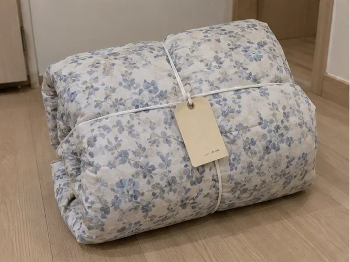 꽃무늬 이불을 단단히 접어 끈으로 묶고 눈에 잘 띄는 태그를 부착한 모습
