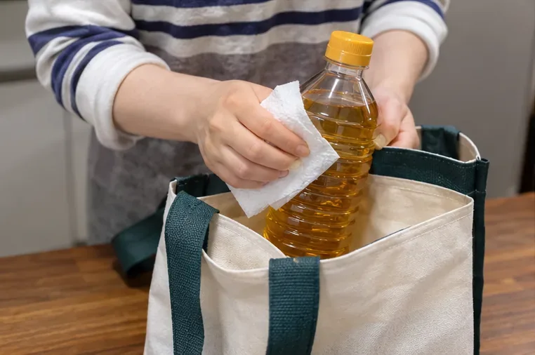 뚜껑을 닫은 폐식용유 병의 겉면을 종이타월로 닦고 장바구니에 넣는 모습
