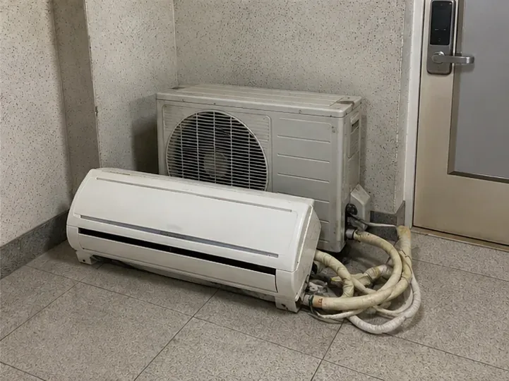 철거된 벽걸이 에어컨 실내기와 실외기가 현관 안쪽 바닥에 함께 정리된 모습