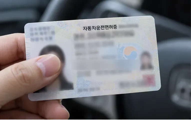 손에 든 운전면허증의 갱신기간을 확인하는 모습. 개인정보와 날짜는 읽을 수 없게 흐려져 있다.