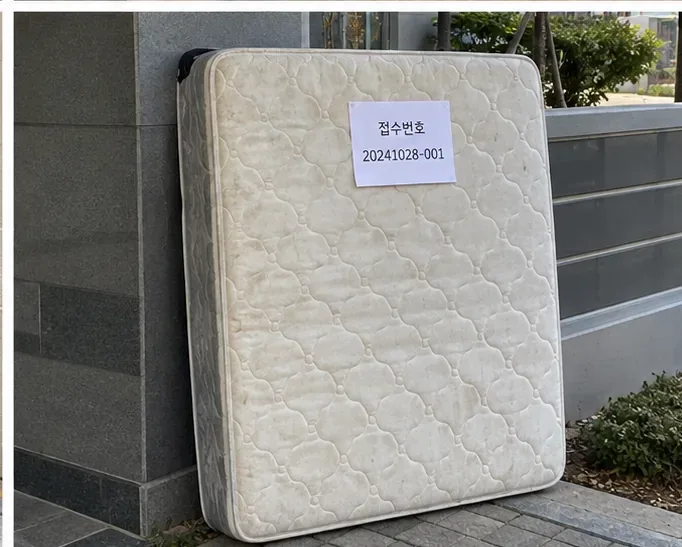 접수번호가 적힌 종이가 부착된 매트리스가 건물 외부 벽면에 세워져 있는 모습