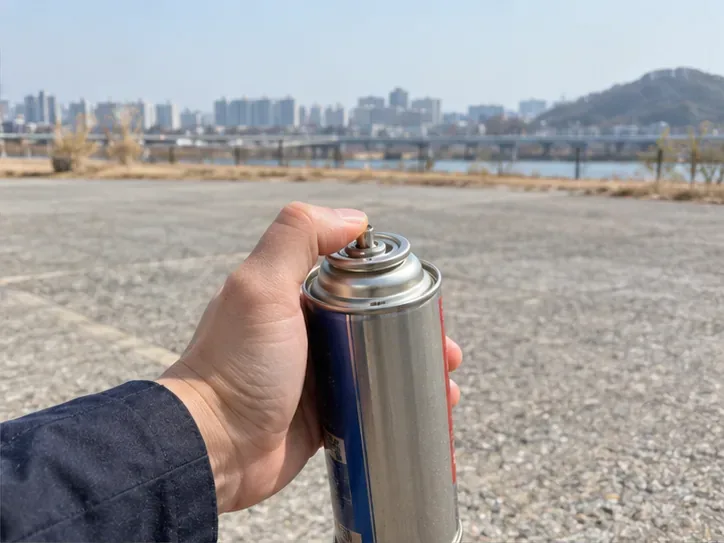 탁 트인 야외에서 부탄 캔의 노즐 부분을 손가락으로 누르는 손