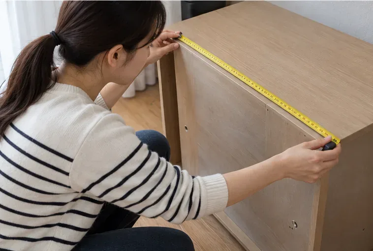 나무 서랍장의 가로 길이를 줄자로 재면서 대형폐기물 규격을 확인하는 모습