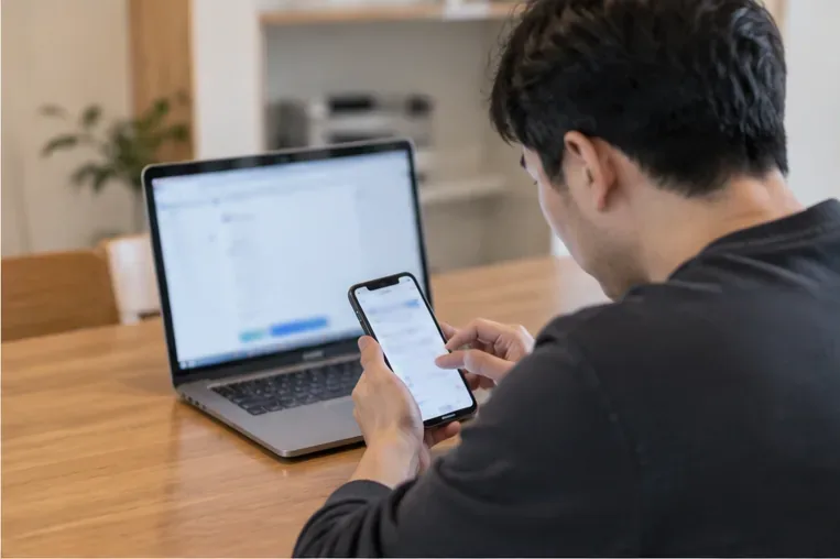 노트북과 휴대전화를 보며 대형폐기물 온라인 신고를 준비하는 사람