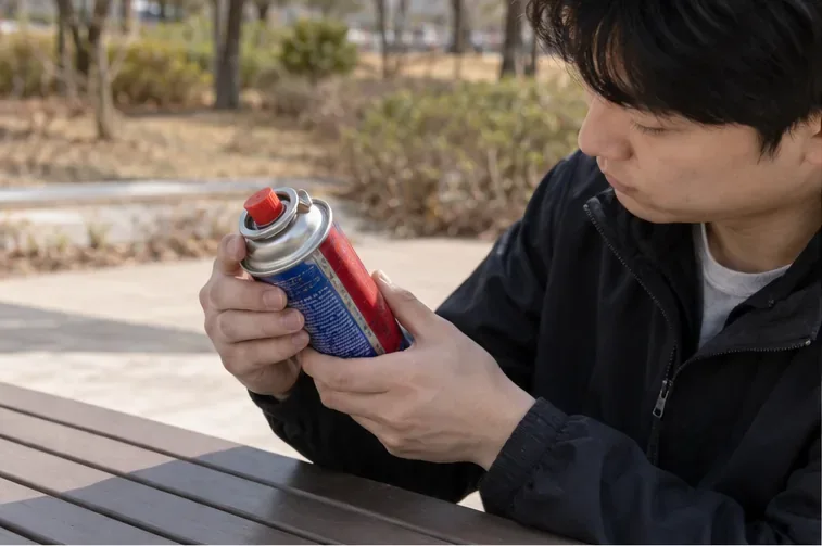야외 테이블에서 휴대용 부탄가스 캔의 노즐과 제품 라벨을 살펴보는 사람