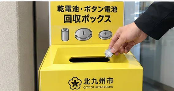 北九州市の電池回収を示す黄色い回収ボックスに小型電池を入れる場面
