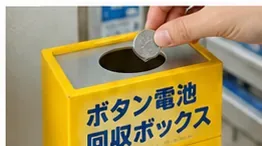 黄色いボタン電池回収ボックスの投入口へ小型の丸い電池を入れようとしている手元