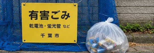 有害ごみの表示があるごみステーション脇に透明袋入りの電池が置かれている様子