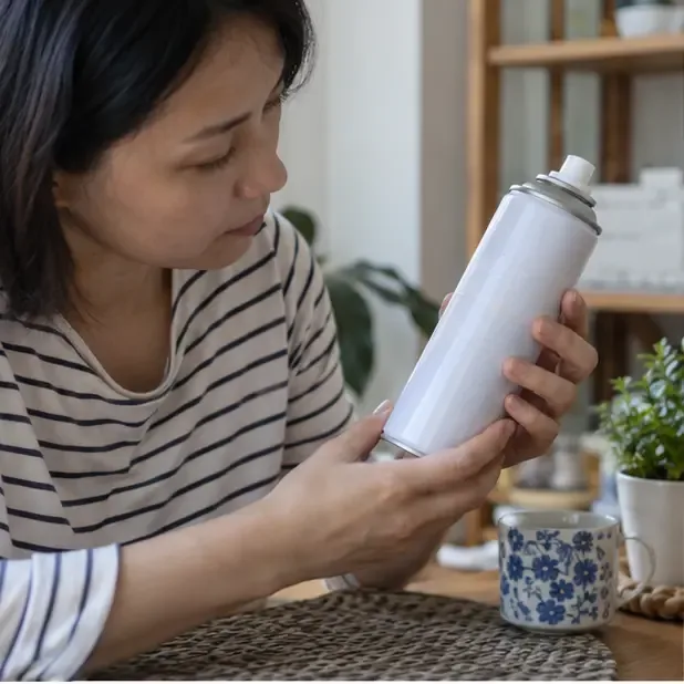 住家室內有人檢查無品牌噴霧罐的外觀與噴頭，先確認罐體是否完整、標示是否可辨識