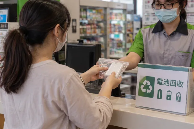 民眾在便利商店櫃台把單獨包裝的行動電源交給店員，旁邊有電池回收標示