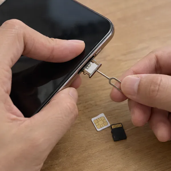 雙手使用取卡針從手機側邊取出 SIM 卡匣，旁邊放著 SIM 卡與記憶卡