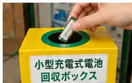 手に持った小型充電池を黄色い小型充電式電池回収ボックスの投入口へ入れている様子