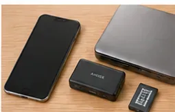 スマートフォン、ノートパソコン、モバイルバッテリー、小型の充電池が木製の机に並んでいる様子