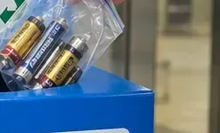 使用済み乾電池を入れた透明袋を青い回収容器の投入口へ静かに入れようとしている手元