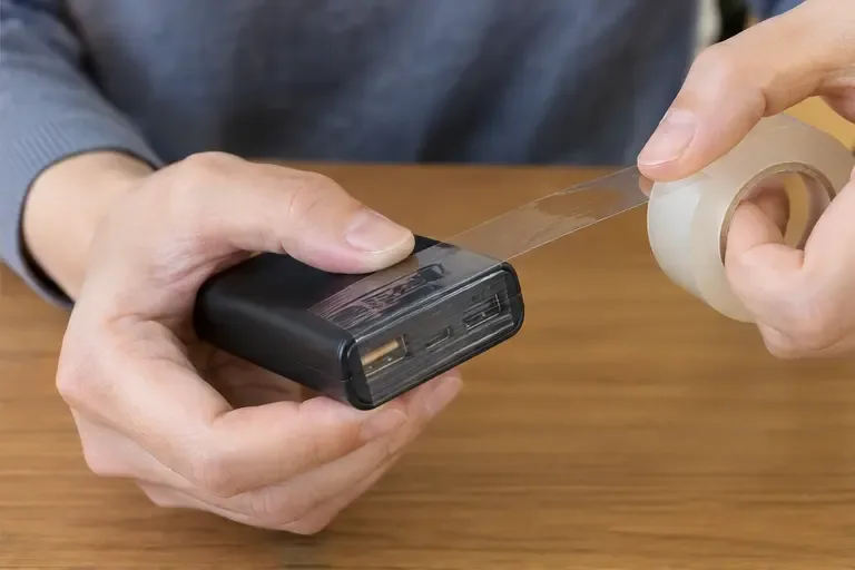 黒いモバイルバッテリーのUSB端子部分に透明テープを貼って絶縁している手元