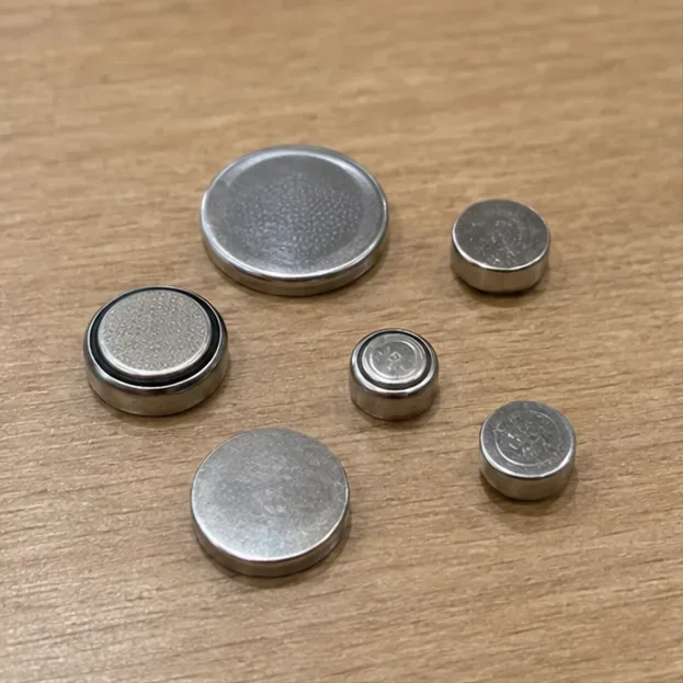 木のテーブルの上に大きさの異なる銀色のボタン形・コイン形電池が並んでいる様子