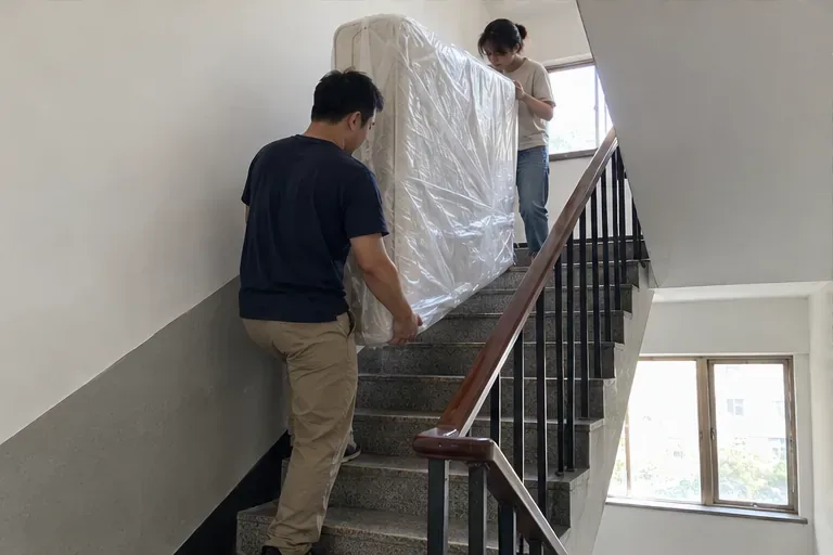 兩名住戶合力將包覆的床墊直立搬下樓梯；宜蘭縣規定巨大垃圾交付前須自行搬至地面樓層，清潔隊不負責進屋搬運。