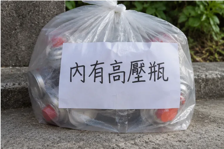 裝有多支空卡式瓦斯罐的透明袋，外側貼著寫有內有高壓瓶的白色警示紙