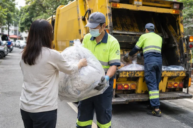 住戶將已裝袋的棉被交給垃圾車旁的清潔人員