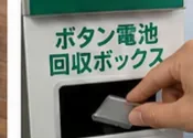 店頭のボタン電池回収ボックスに、手で小さな丸い電池を入れようとしている様子