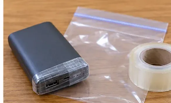 黒いモバイルバッテリーのUSB端子周辺を透明なテープで覆い、横に透明袋を用意している様子