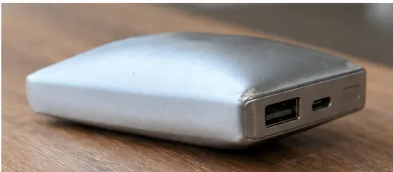 木製の机の上でケース中央が大きく盛り上がり、外装が変形した銀色のモバイルバッテリー