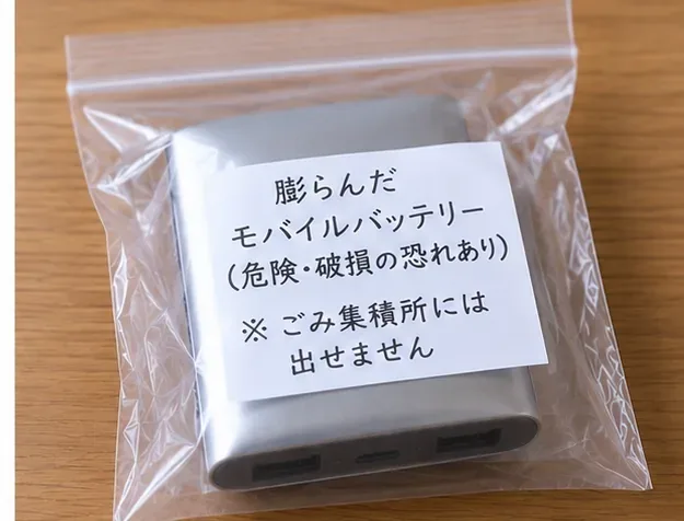 膨らんだモバイルバッテリーを透明な袋の中で他の物と分けて置き、「ごみ集積所には出せません」と注意書きを添えた状態