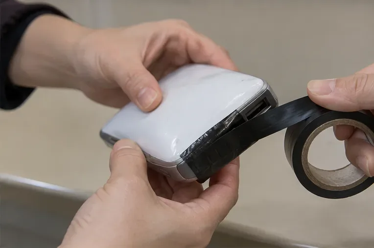 膨らんだモバイルバッテリーの接続端子側を黒い絶縁テープで覆っている手元