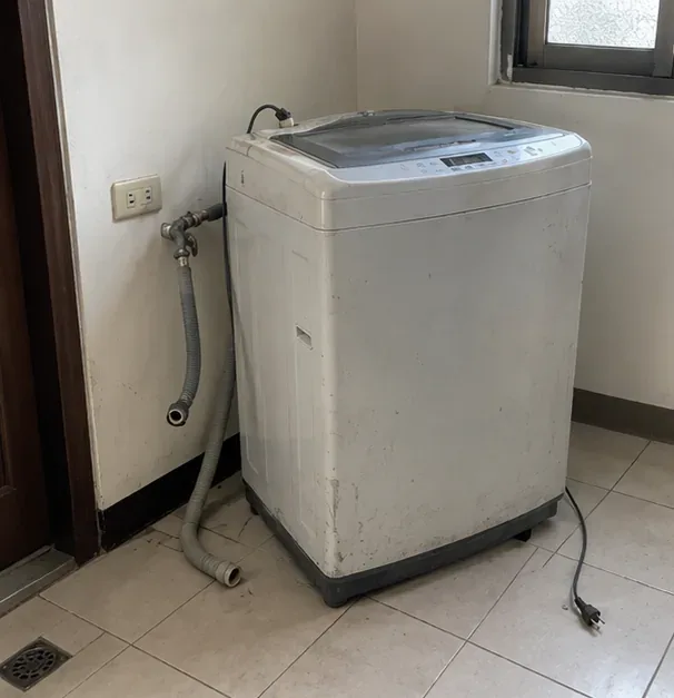 住家洗衣空間內一台已拔除電源、排水管與進水管的舊直立式洗衣機