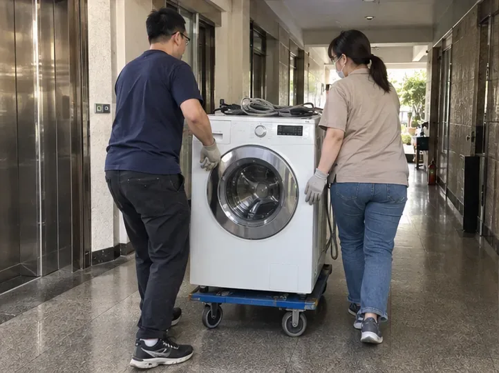 兩名成人用推車在大樓走廊搬運已固定水管與電線的洗衣機