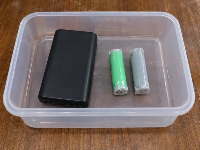 透明塑膠容器內放著一個黑色行動電源和兩顆已貼膠帶的圓柱形電池。