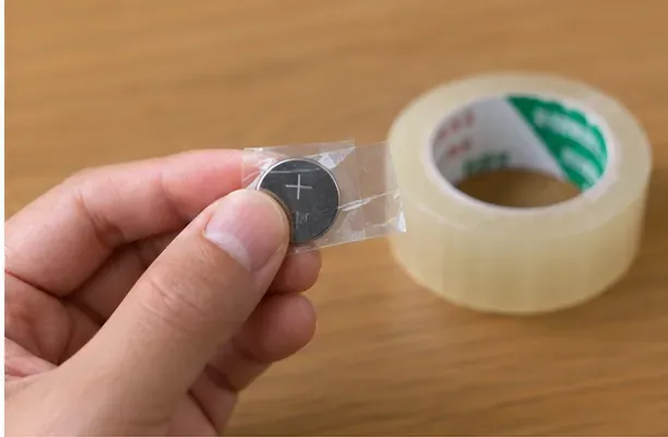 小型の丸い電池を透明テープで覆って絶縁している手元