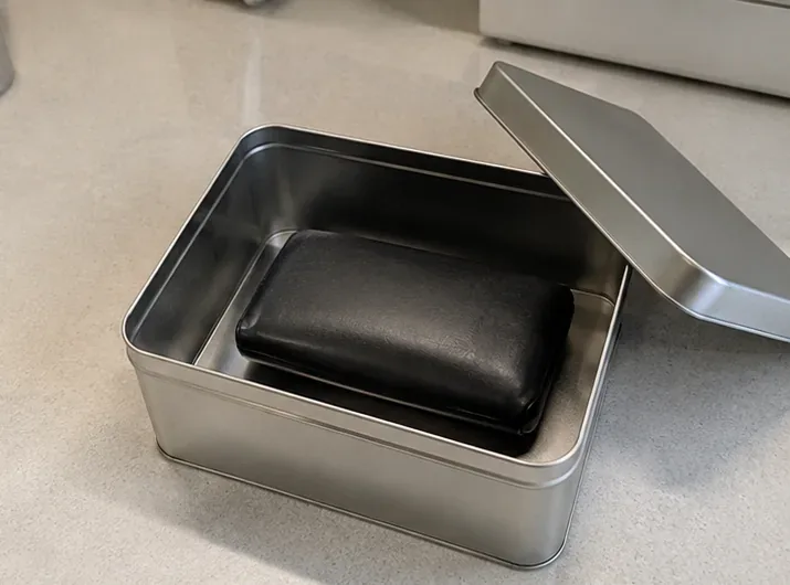 膨らんだ黒いモバイルバッテリーを金属製の容器に入れ、ふたを閉じる前の状態