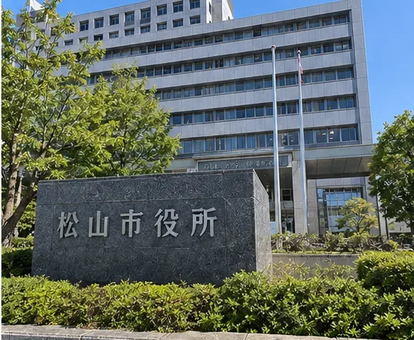 晴天時の松山市役所庁舎と松山市役所と刻まれた石碑