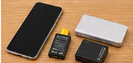 スマートフォン、モバイルバッテリー、取り外し可能な小型バッテリーパックが木製の机に並んでいる様子